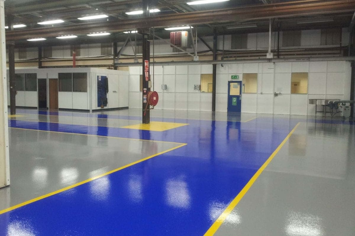 Clean industrial warehouse featuring glossy grey and blue epoxy flooring with yellow safety lines.