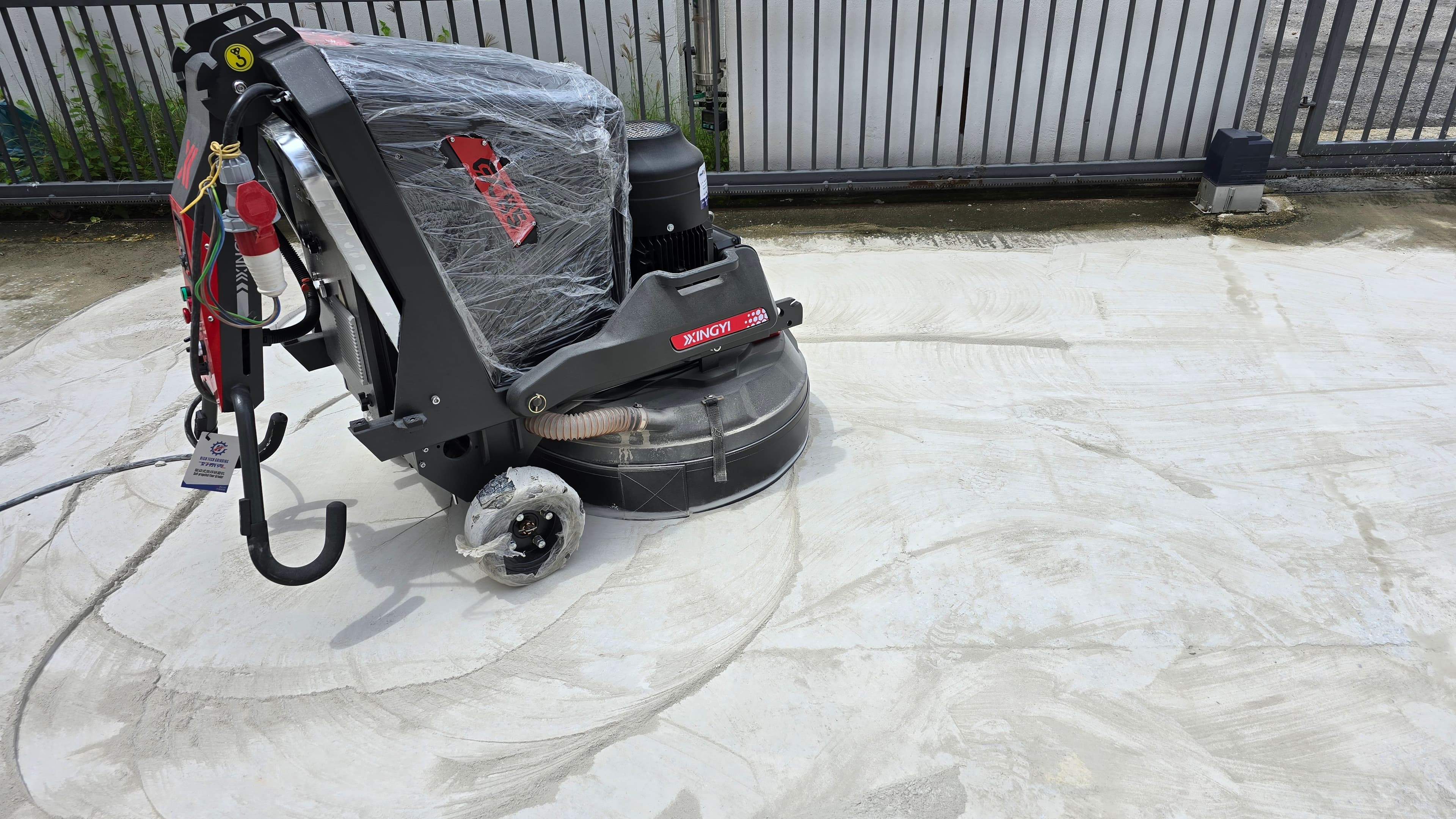 Xingyi industrial floor grinder on a concrete surface with visible swirl marks near a fence.