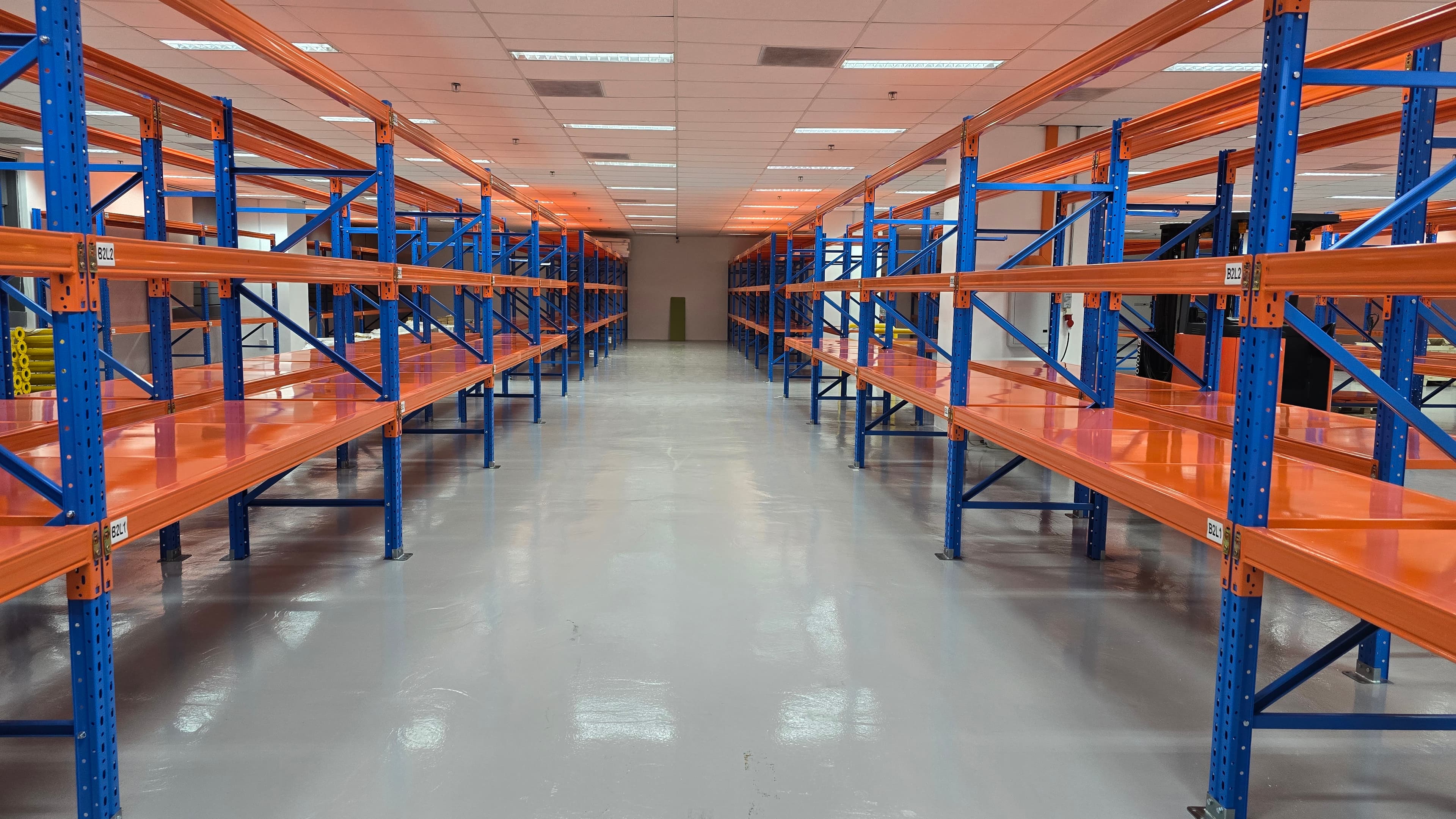 Empty blue and orange industrial shelving units lining a clean, brightly lit warehouse aisle.