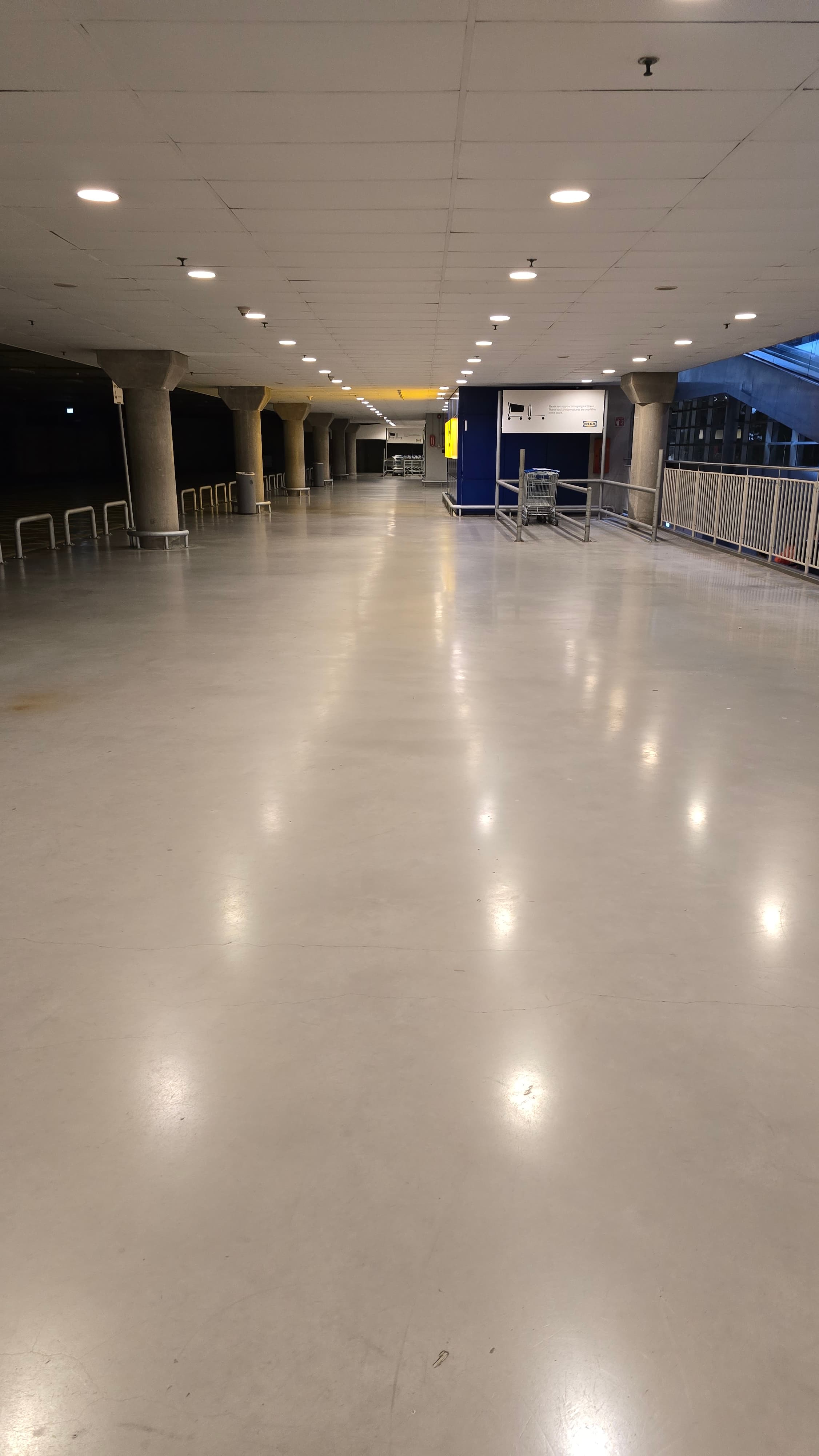 Empty industrial hallway with polished concrete floors, concrete pillars, and bright overhead lights.