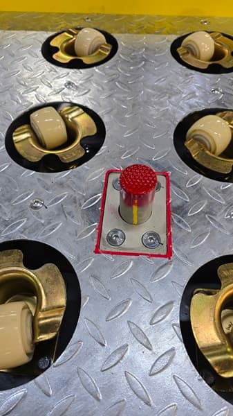 Metal diamond plate surface with recessed rollers and a central red emergency stop button.