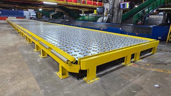 Long industrial ball transfer table with yellow metal framing in a large cargo handling facility.
