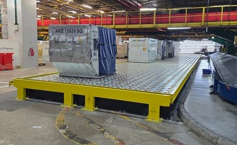 Large cargo containers resting on a yellow roller deck platform in an airport facility.