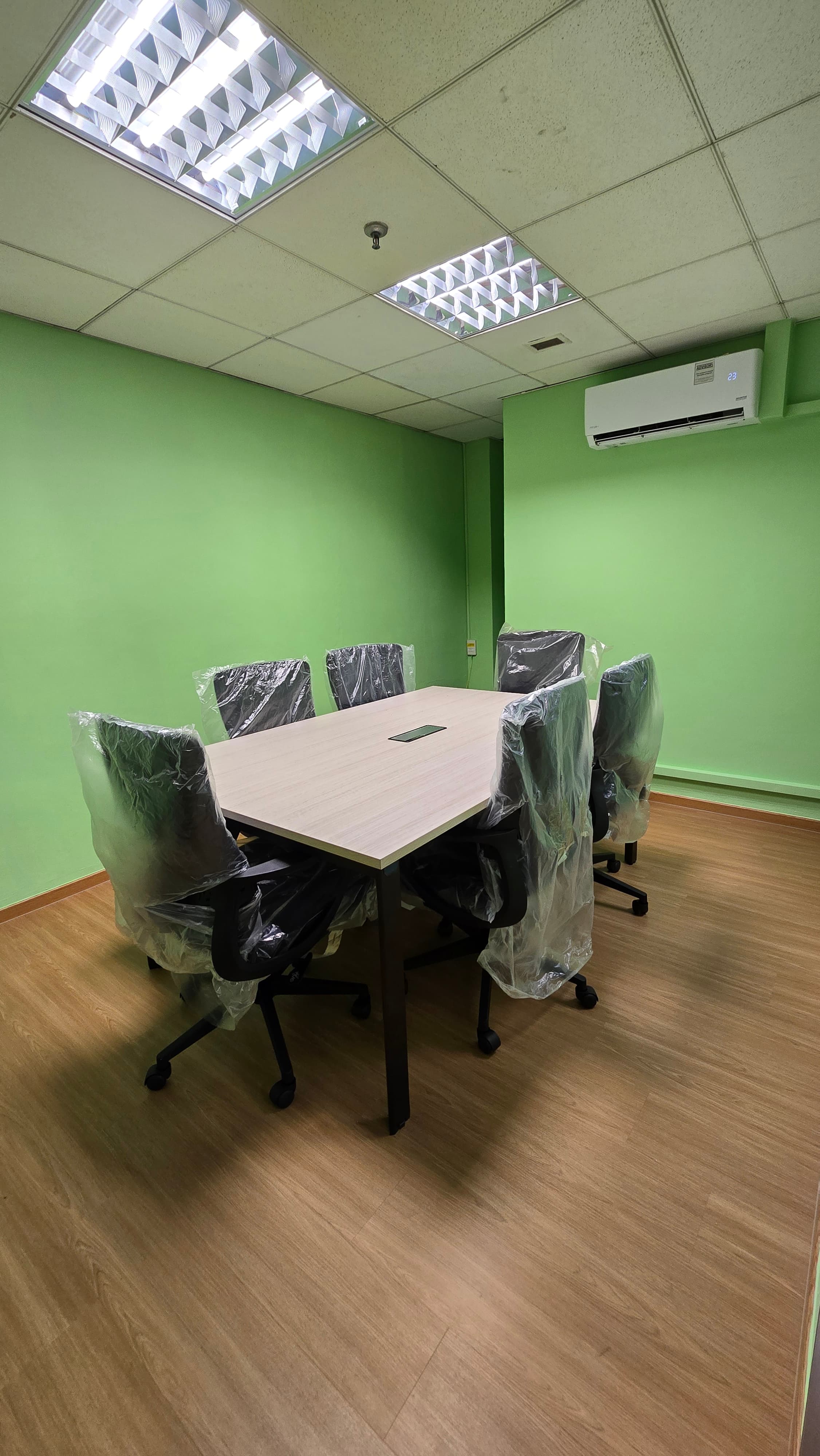 Six black chairs wrapped in plastic around a wooden table in a green meeting room.