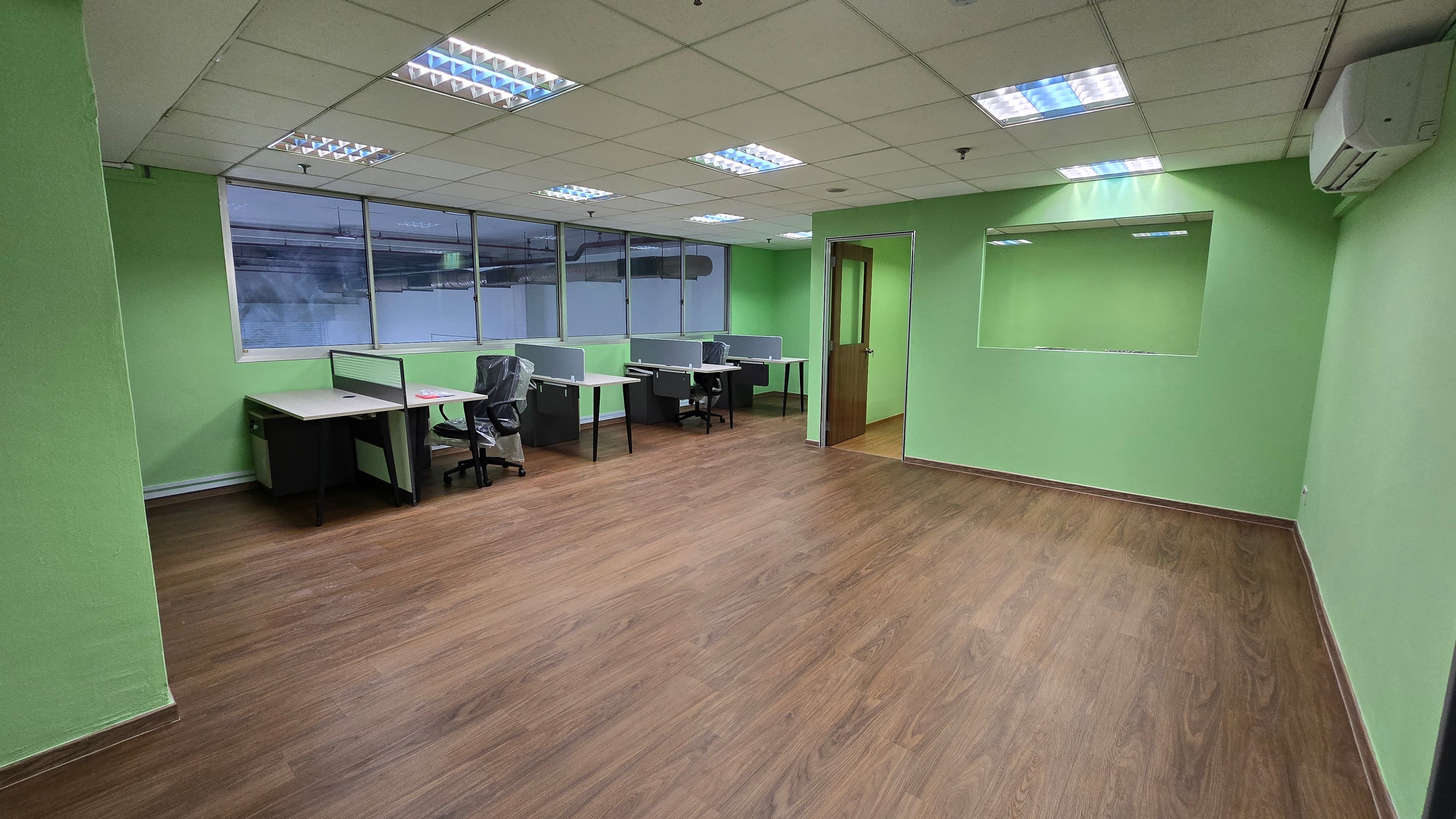 Empty office featuring lime green walls, wood flooring, and several workstations arranged near large windows.