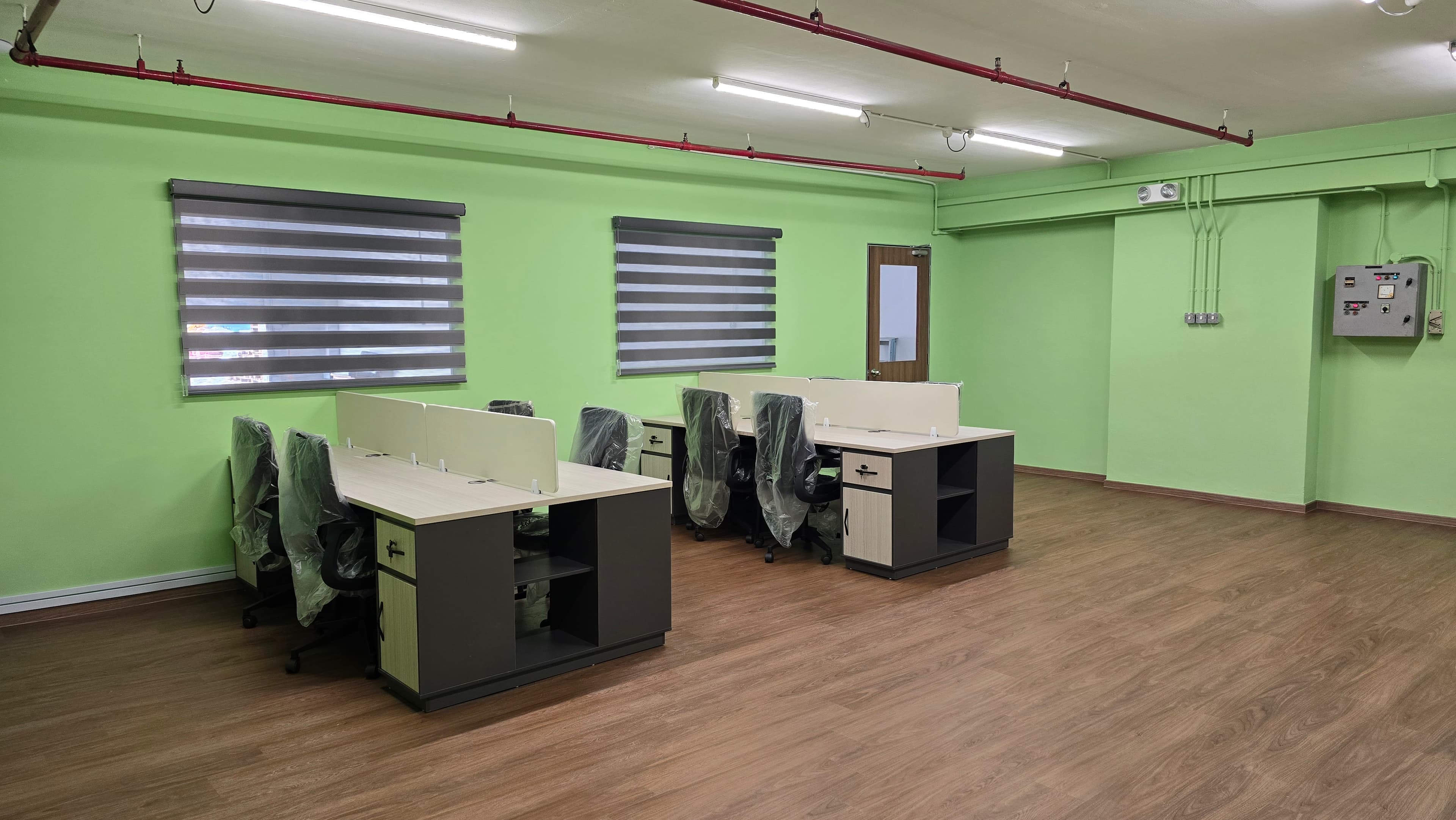 Modern office with lime green walls, new desks, plastic-wrapped chairs, and wooden floors.