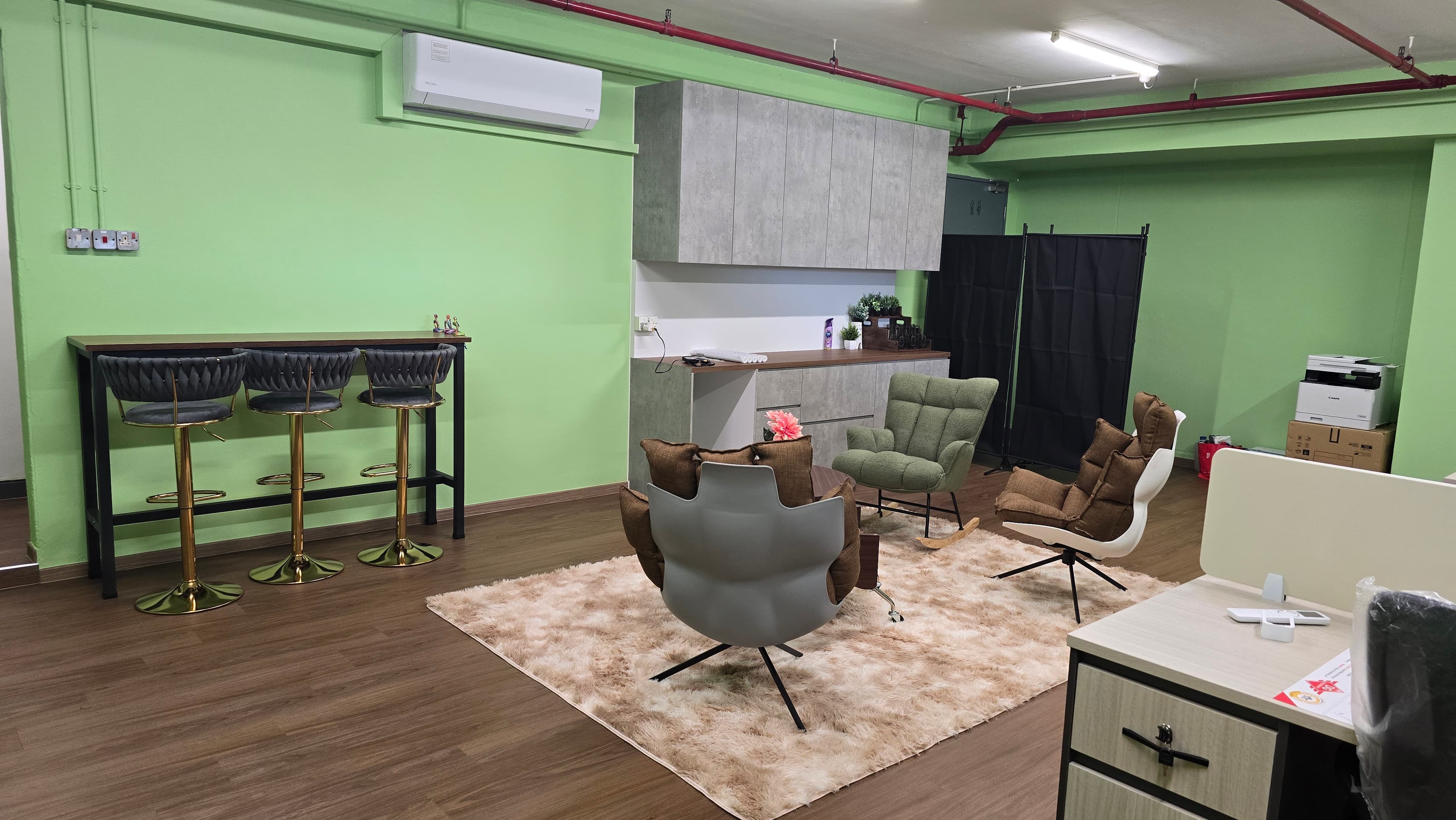 Modern office lounge featuring green walls, bar stools, and armchairs on a plush rug.