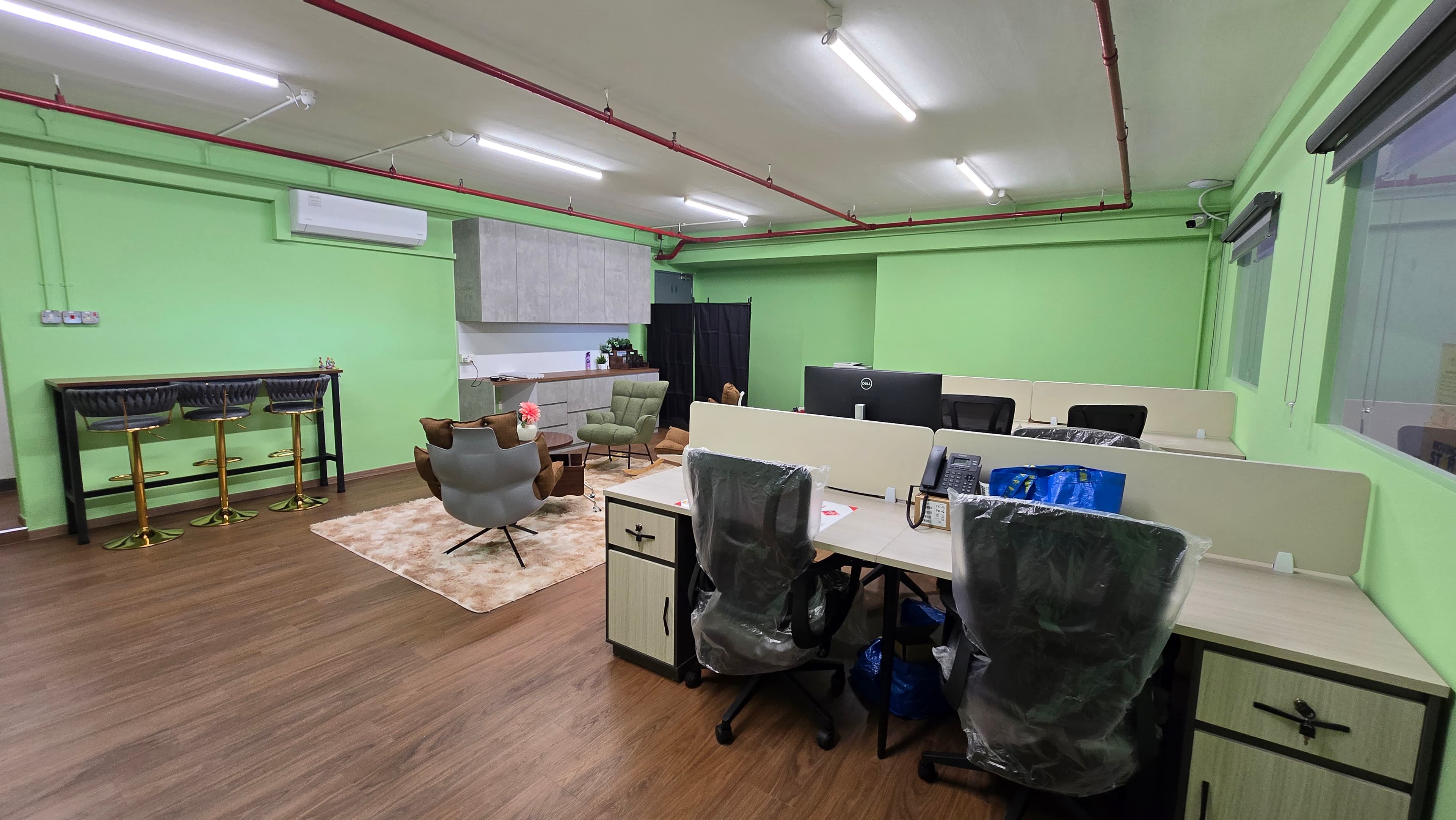 Modern office with green walls, wooden floors, workstations, and a lounge area with plush chairs.