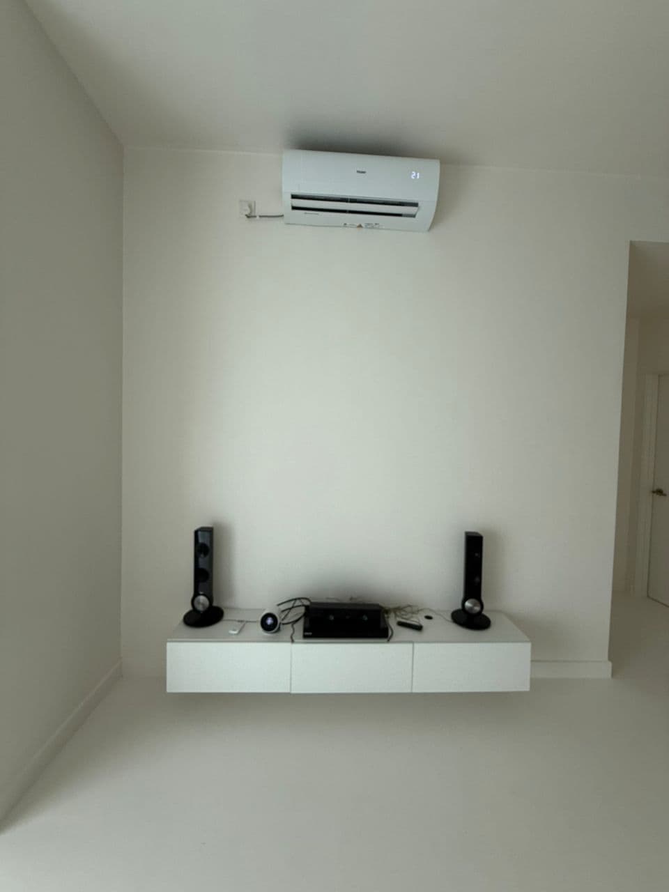 Modern white room with a floating media console, black speakers, and a wall-mounted air conditioner.
