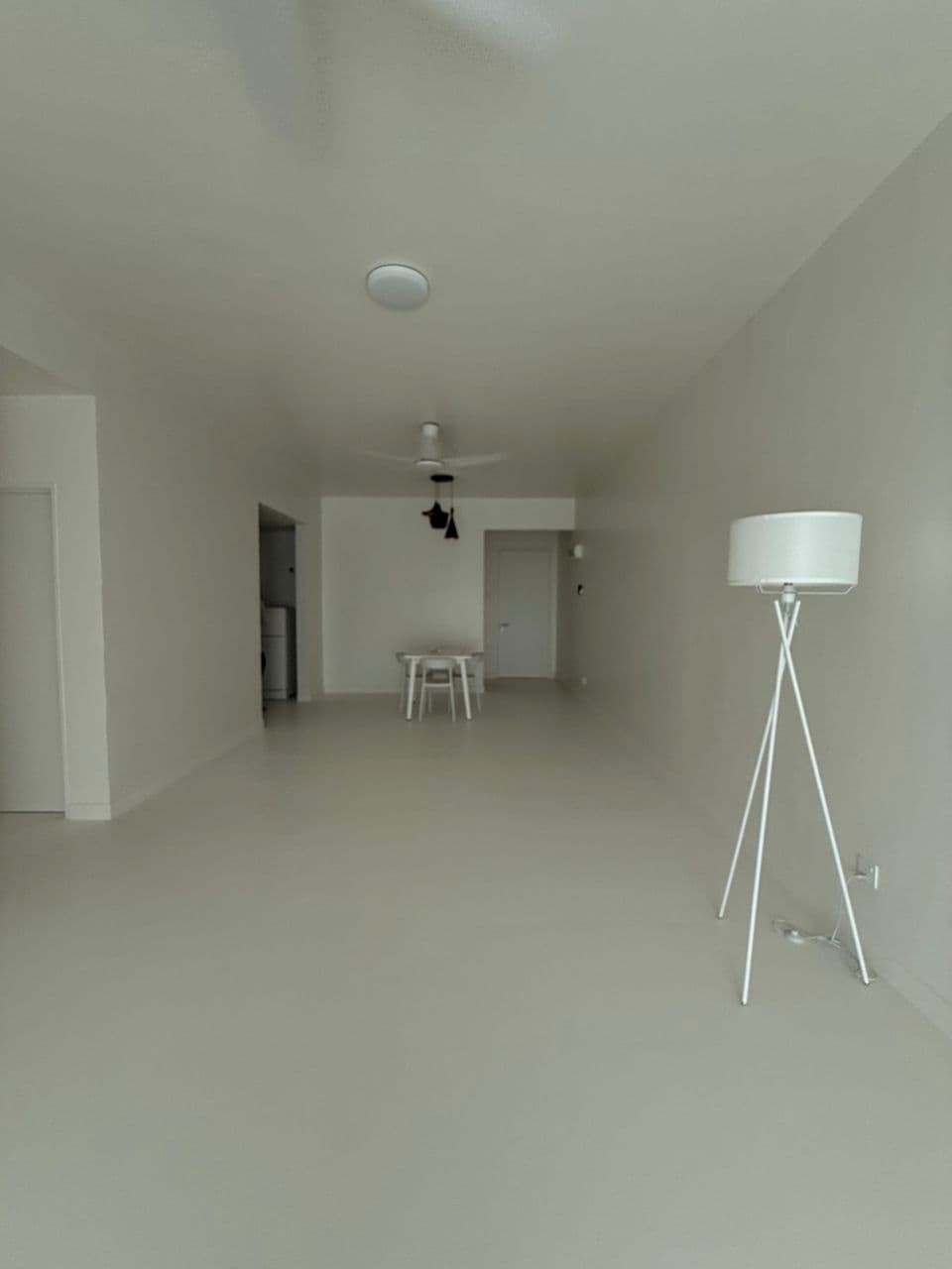 Minimalist white room with a tripod floor lamp and a small white dining table set.