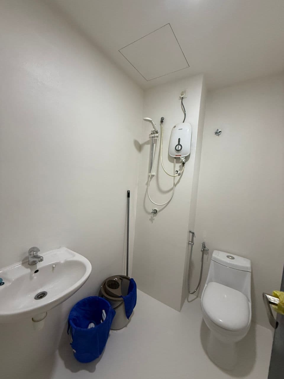 Minimalist white bathroom featuring a sink, toilet, and a wall-mounted electric shower heater.