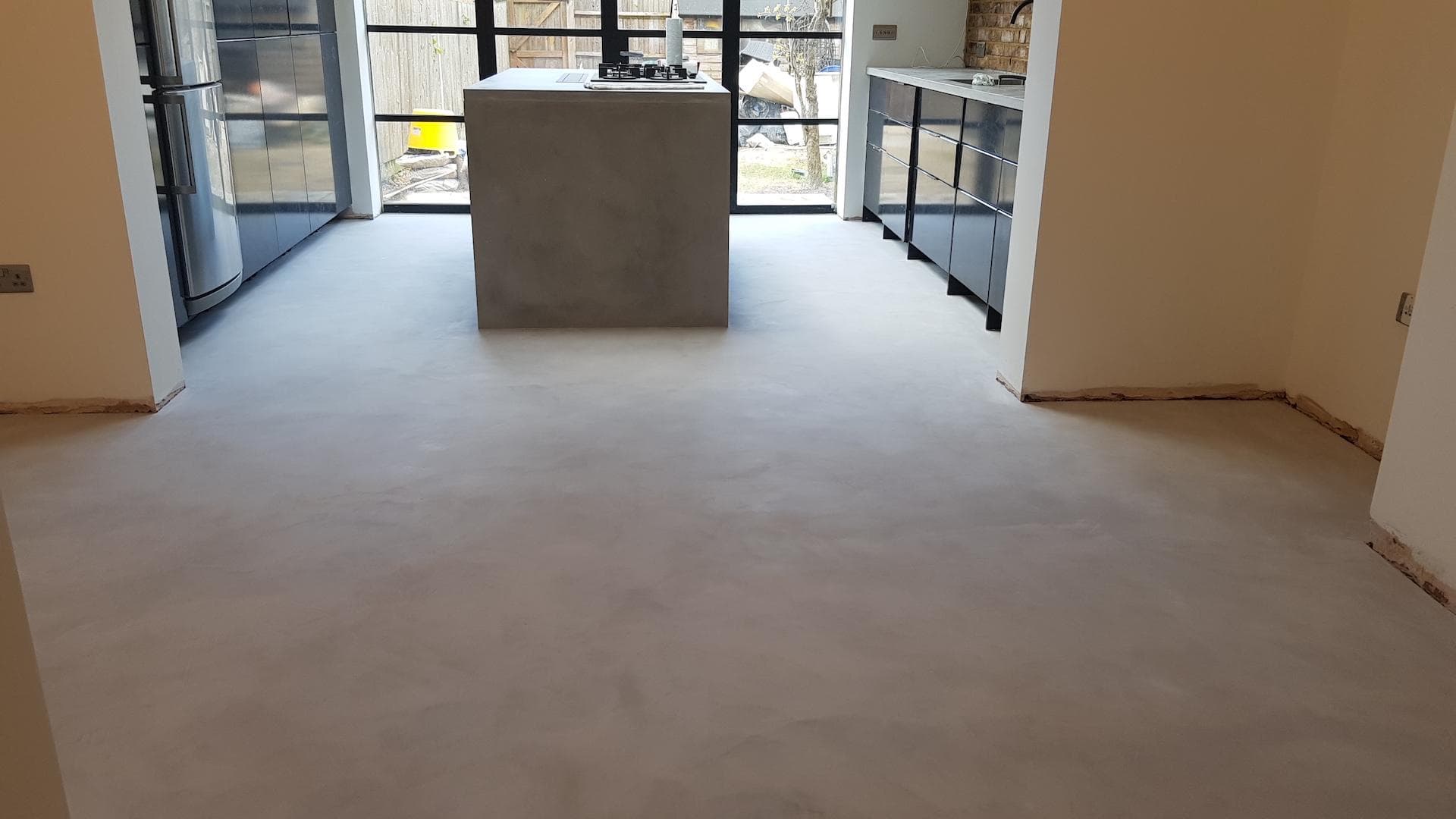 Seamless light gray microcement floor in a modern kitchen with a matching central concrete island.