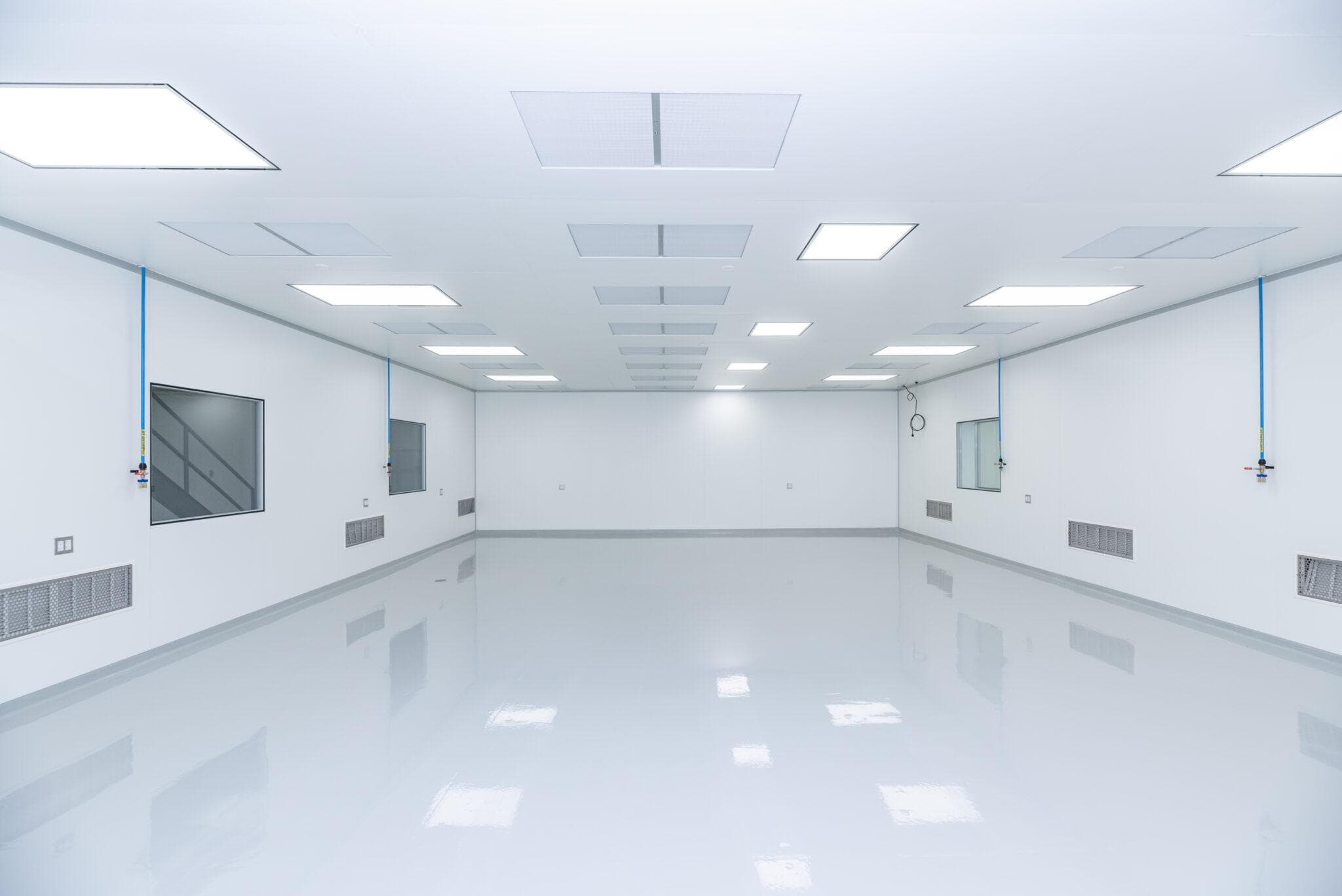 Brightly lit empty sterile cleanroom with white walls, reflective floor, and ceiling light panels.