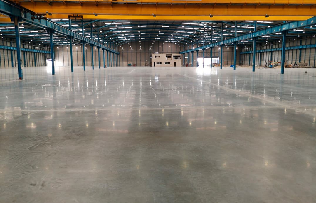 Large empty warehouse with a polished concrete floor reflecting overhead lights and blue steel pillars.