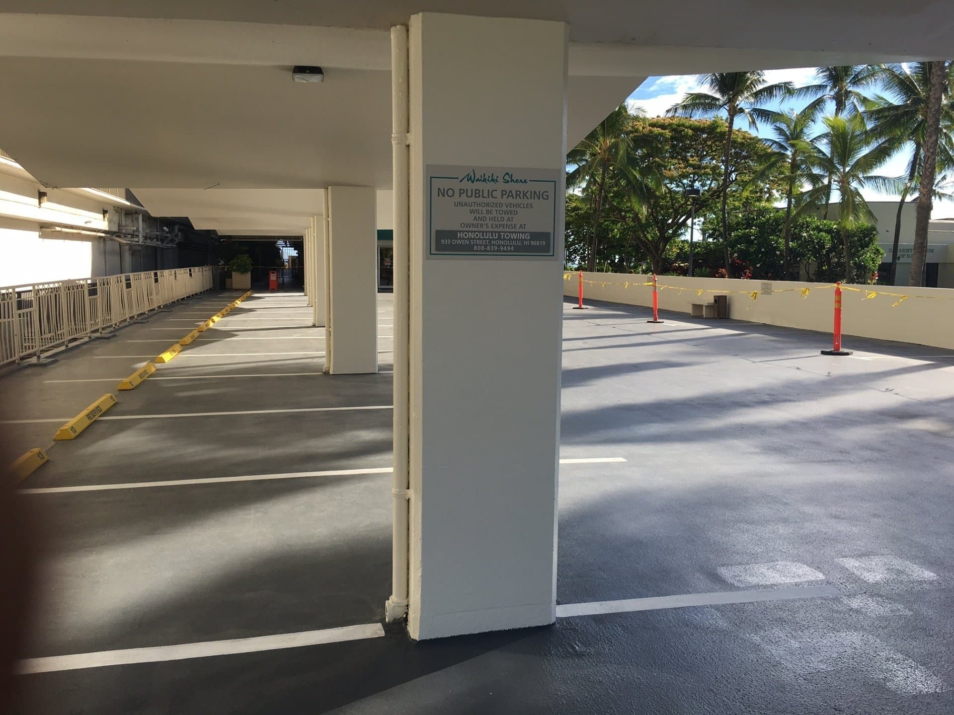 Empty parking garage with a No Public Parking sign on a pillar and palm trees.