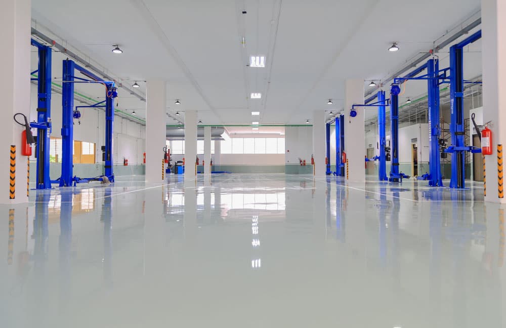 Spacious modern auto repair shop with blue car lifts and a glossy reflective floor.