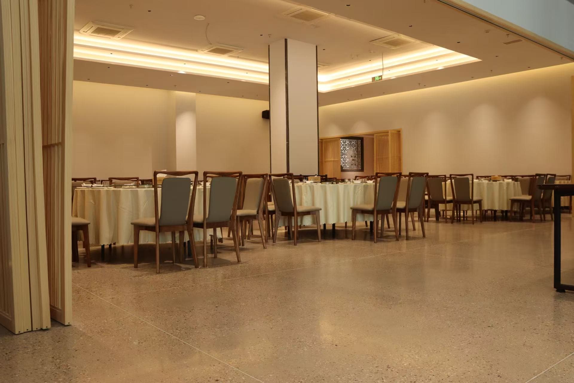 Spacious dining room with round tables, wooden chairs, and warm recessed lighting on polished floors.