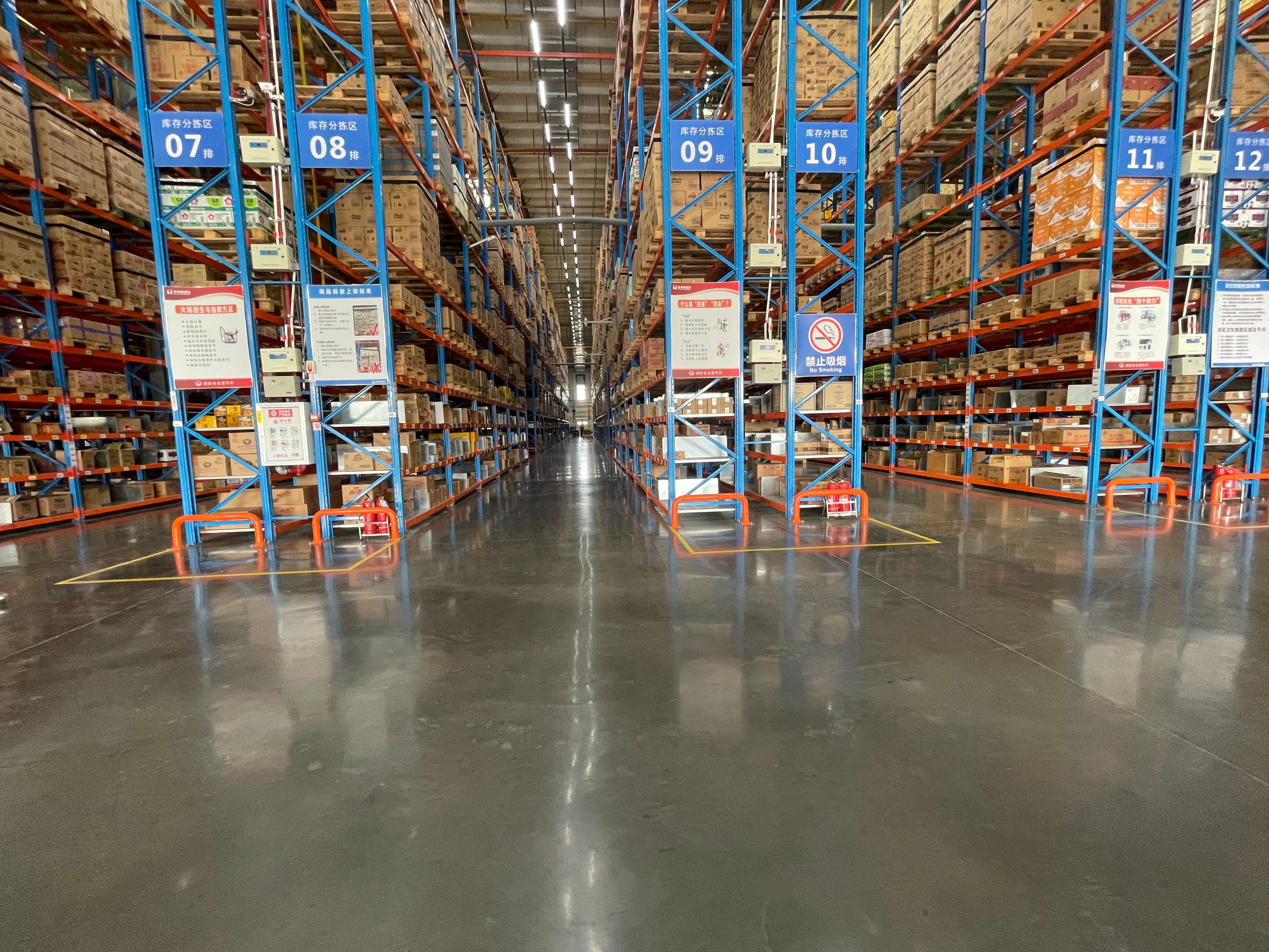 Numbered blue storage racks filled with boxes in a large warehouse with reflective floors.