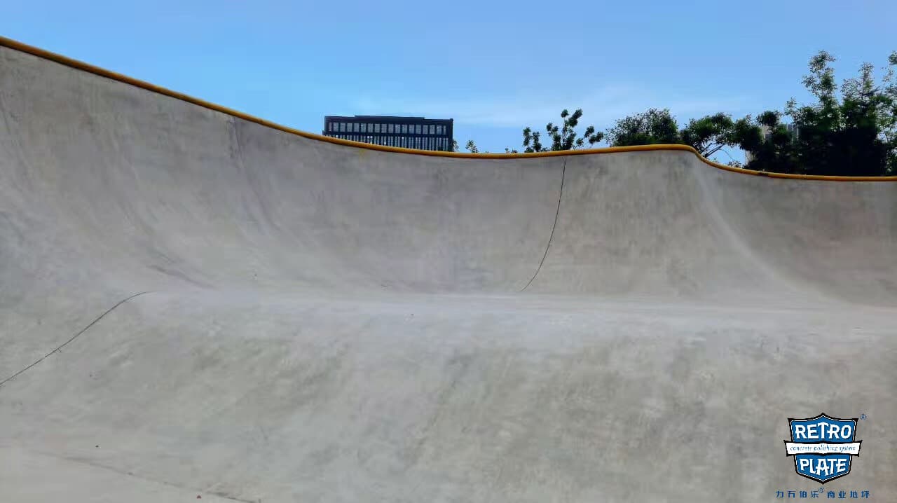 Smooth polished concrete skatepark bowl with yellow coping under a clear blue sky.