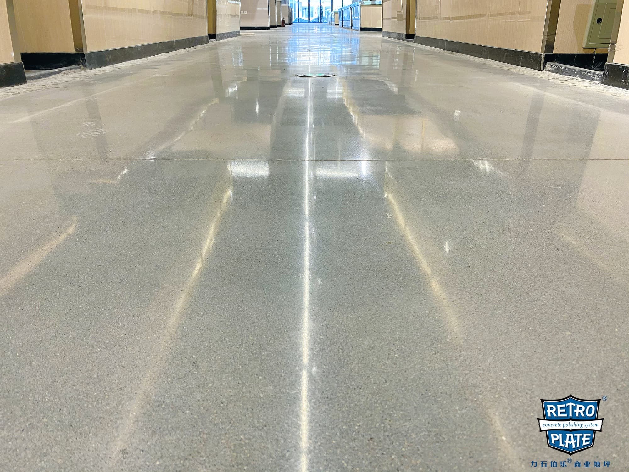 Polished grey concrete floor in a long hallway reflecting overhead lights and beige walls.
