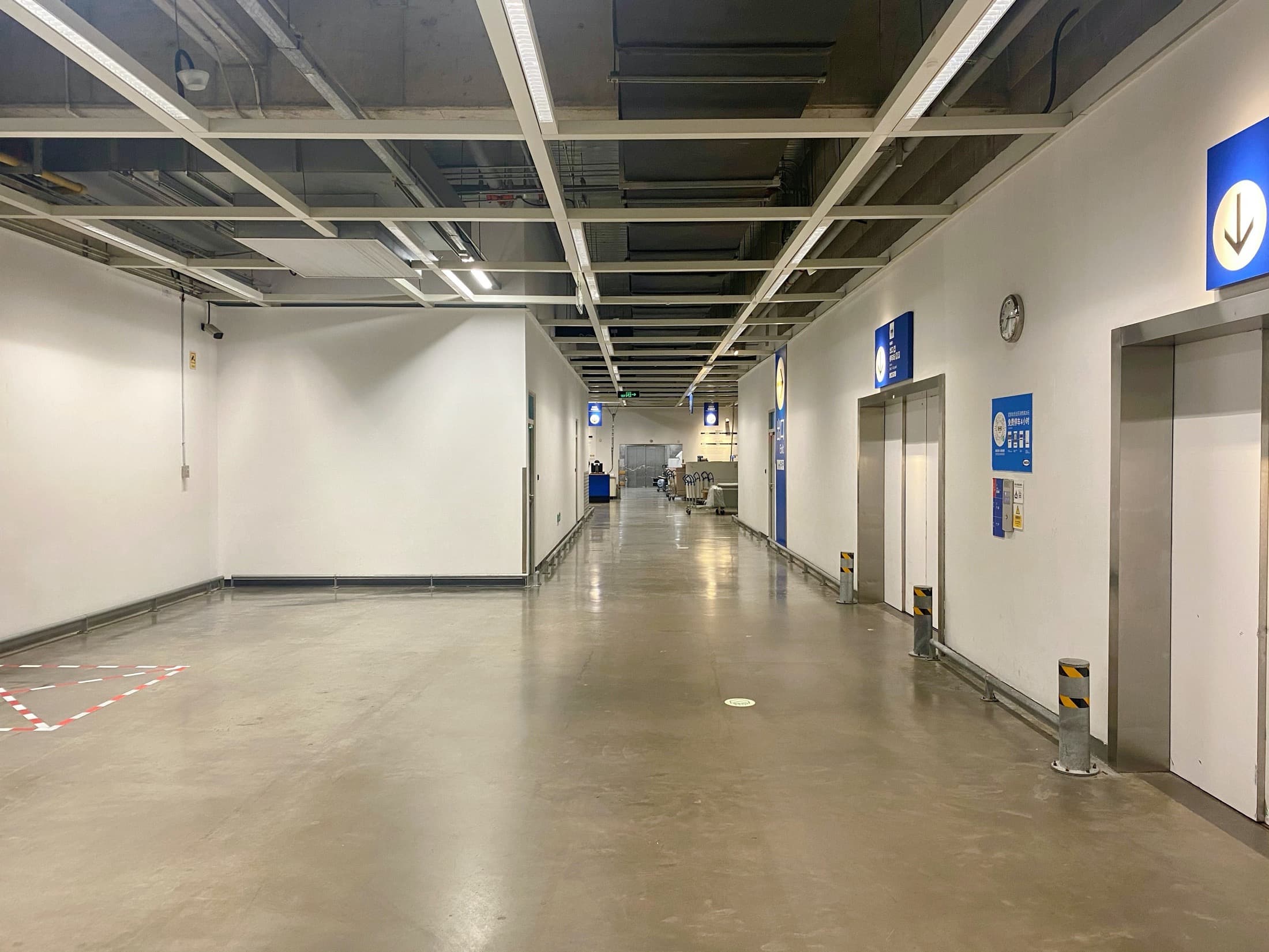 Empty industrial corridor with polished concrete floors, white walls, and elevators under grid lighting.