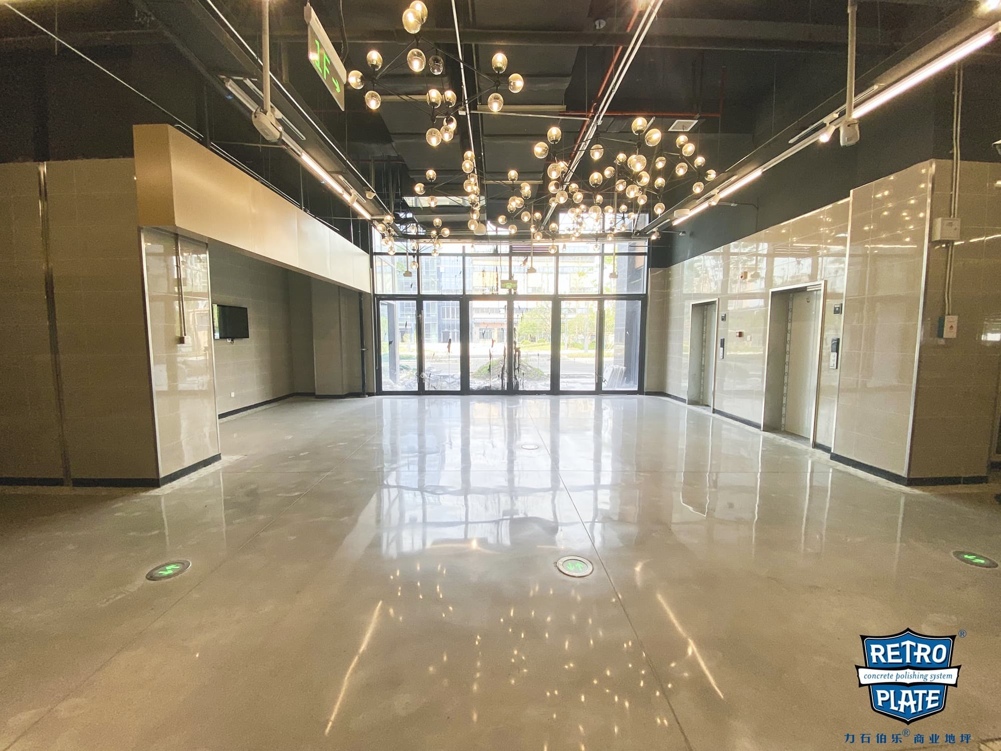 Modern lobby with highly reflective polished concrete floors, industrial ceiling, and hanging globe lights.